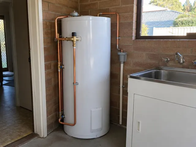New hot water cylinder with copper pipework beside a laundry sink on a brick wall in Jewells