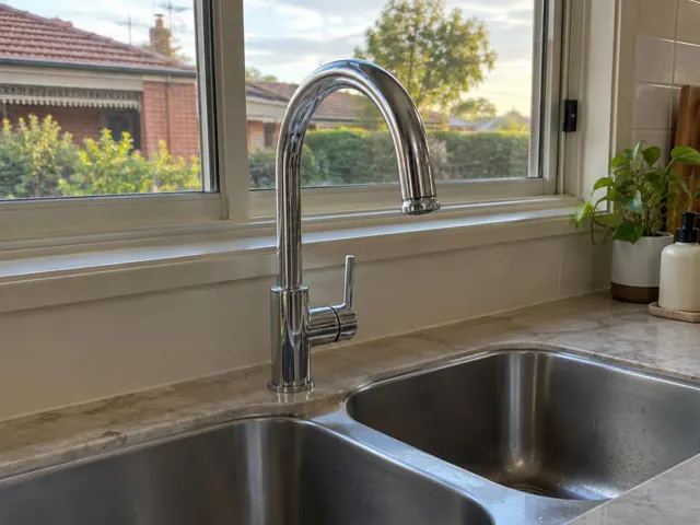 Chrome kitchen mixer tap over double stainless sink beside a window and stone benchtop in Redhead