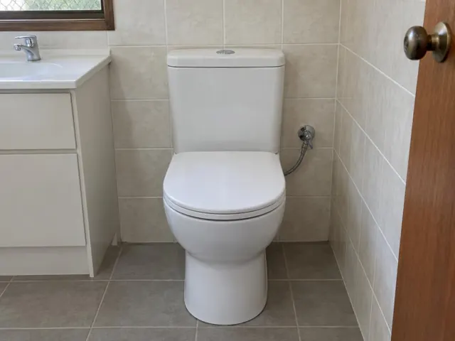 White toilet in a tiled bathroom beside a vanity and timber door in Jewells